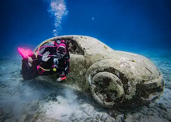 A diver posing with a sculpture by Rodrigo Quinones Reyes of a VW beetle named 'The Anthropocene'.